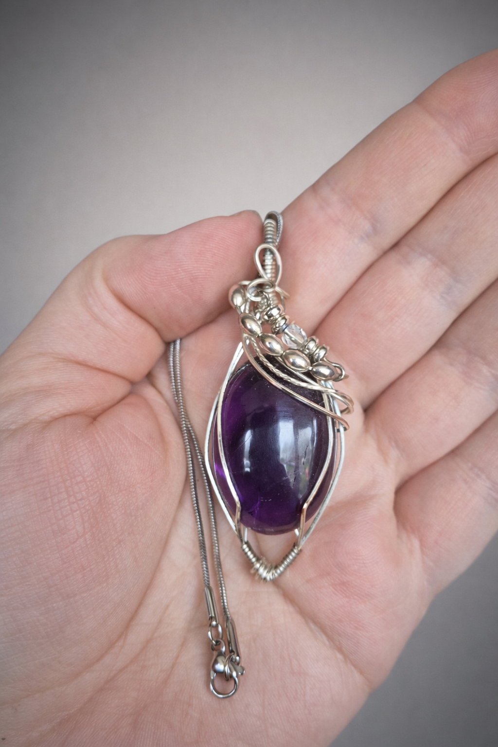 a deep purple amethyst wrapped in silver with decorative swirls and beads on a snake chain